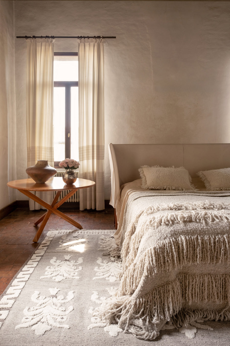 Light grey wool rug with hand-knotted floral-inspired motifs in a calm, natural bedroom.