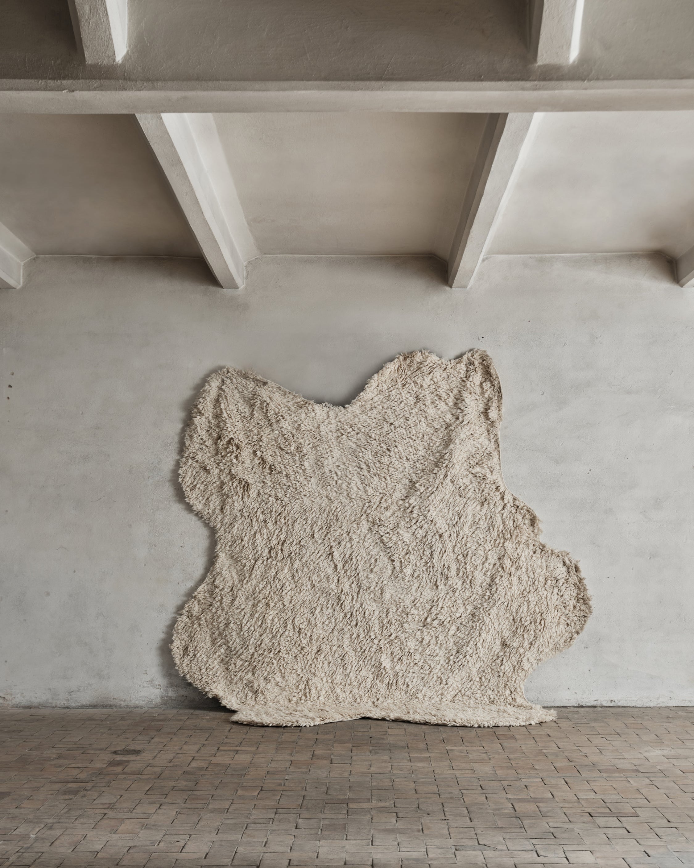 A shaggy, off-white wool rug with an organic and irregular shape. Handmade in natural wool, providing a soft and artistic statement piece.